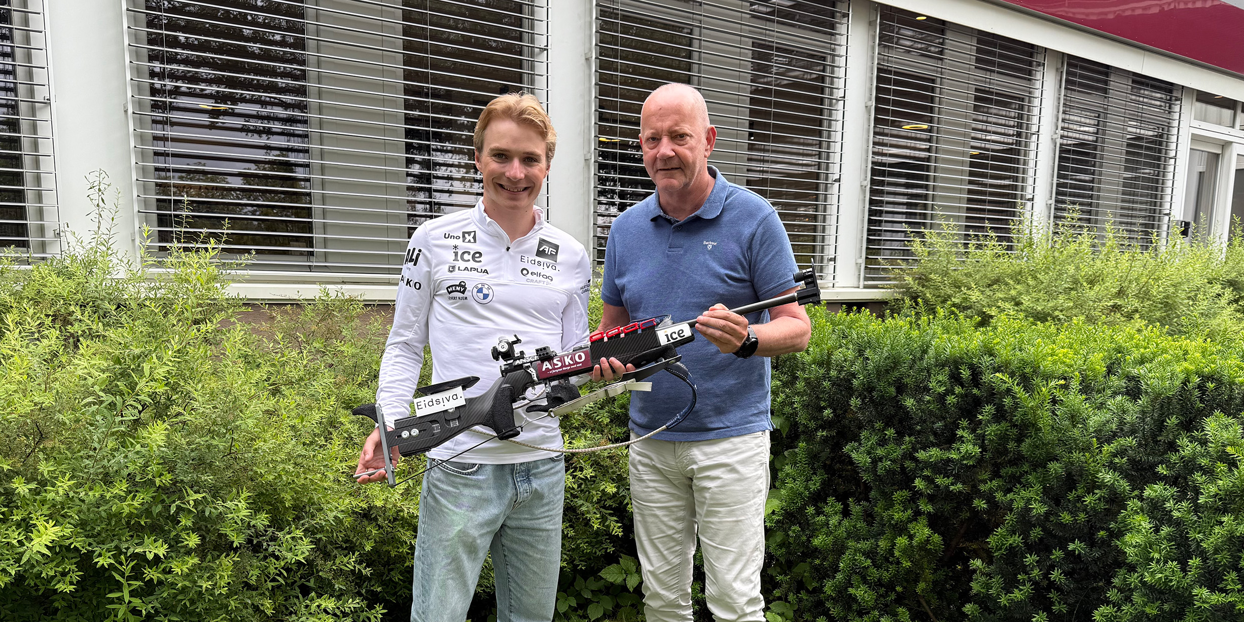 Isak Frey og Tore Bekken står foran ASKO-bygg i Oslo og holder et skiskyttergevær