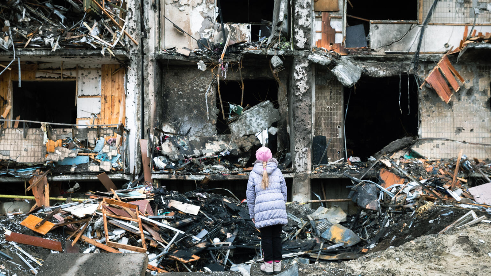 En liten jente som står foran en bygning som er sprengt