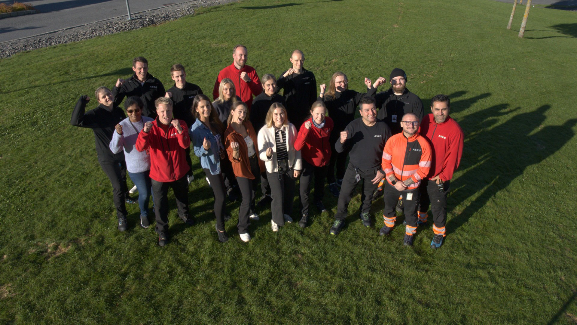 Kvinner og menn som er ansatt hos ASKO SENTRALLAGER og TRANSPORT smiler på gresset.